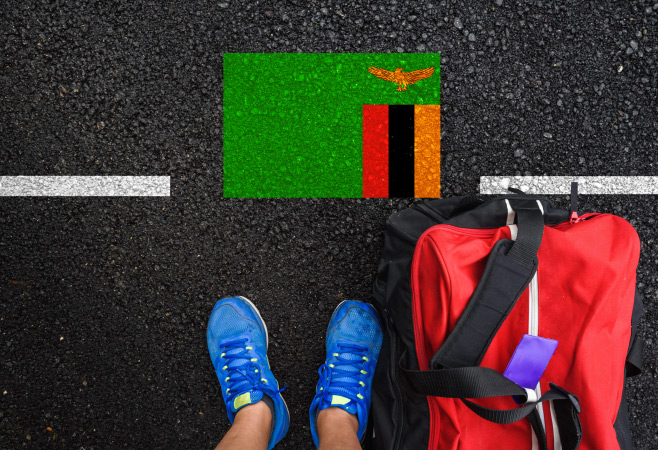 A man is standing on asphalt next to flag of Zambia and border