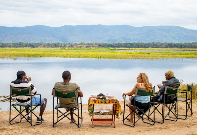 People sitting on camping chairs looking at the Zambezi having breakfast